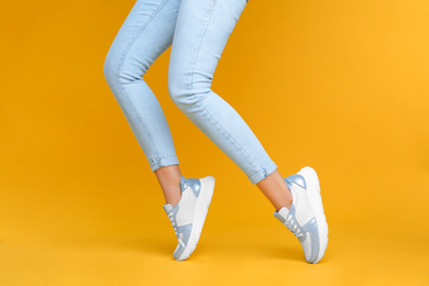 Woman wearing stylish sneakers on yellow background, closeup