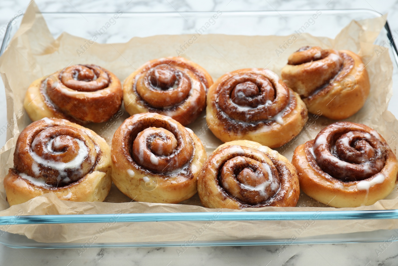 Photo of Baking dish with tasty cinnamon rolls on white marble table, closeup