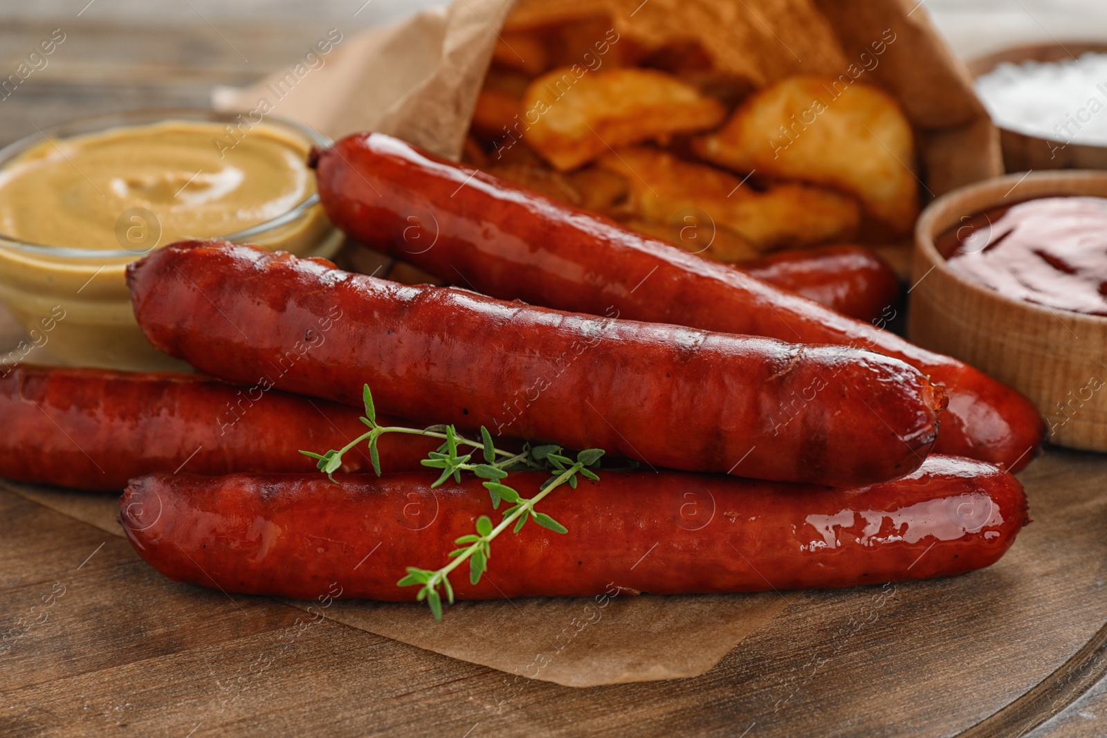 Photo of Delicious grilled sausages and sauces on wooden board, closeup. Barbecue food