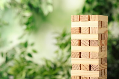 Photo of Jenga tower made of wooden blocks outdoors. Space for text