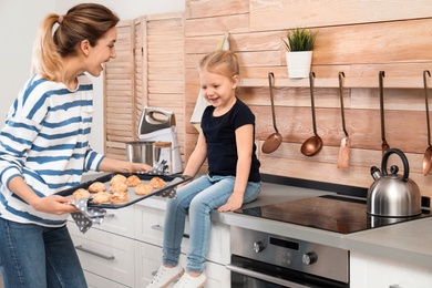 Photo of Young woman treating her daughter with homemade oven baked cookies in kitchen
