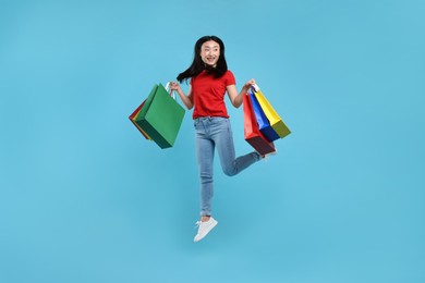 Happy woman jumping with shopping bags on light blue background