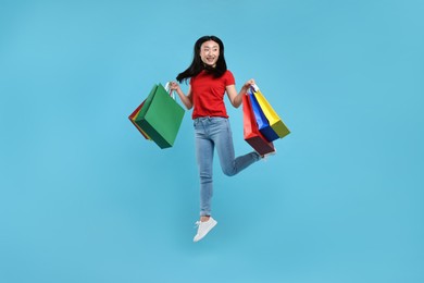 Photo of Happy woman jumping with shopping bags on light blue background