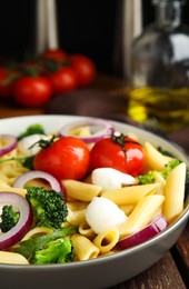 Bowl of delicious pasta with tomatoes, onion and broccoli on wooden table, closeup