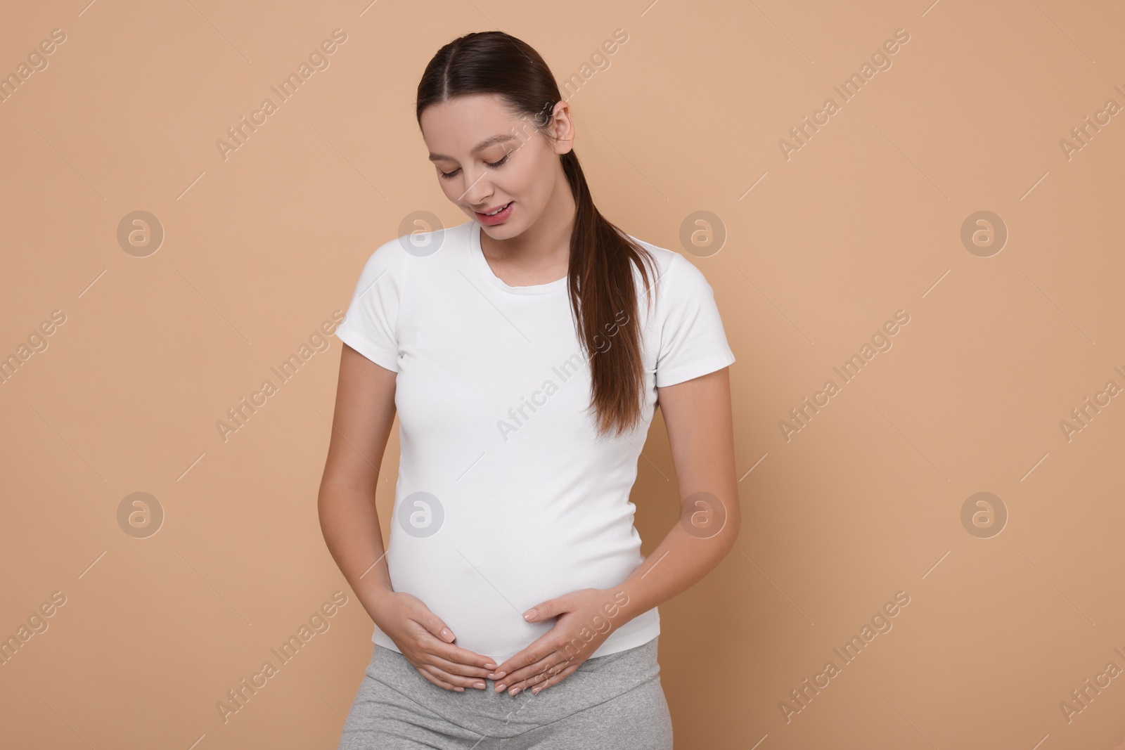 Photo of Beautiful pregnant woman in white T-shirt on beige background