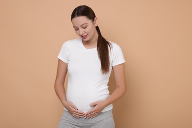 Beautiful pregnant woman in white T-shirt on beige background