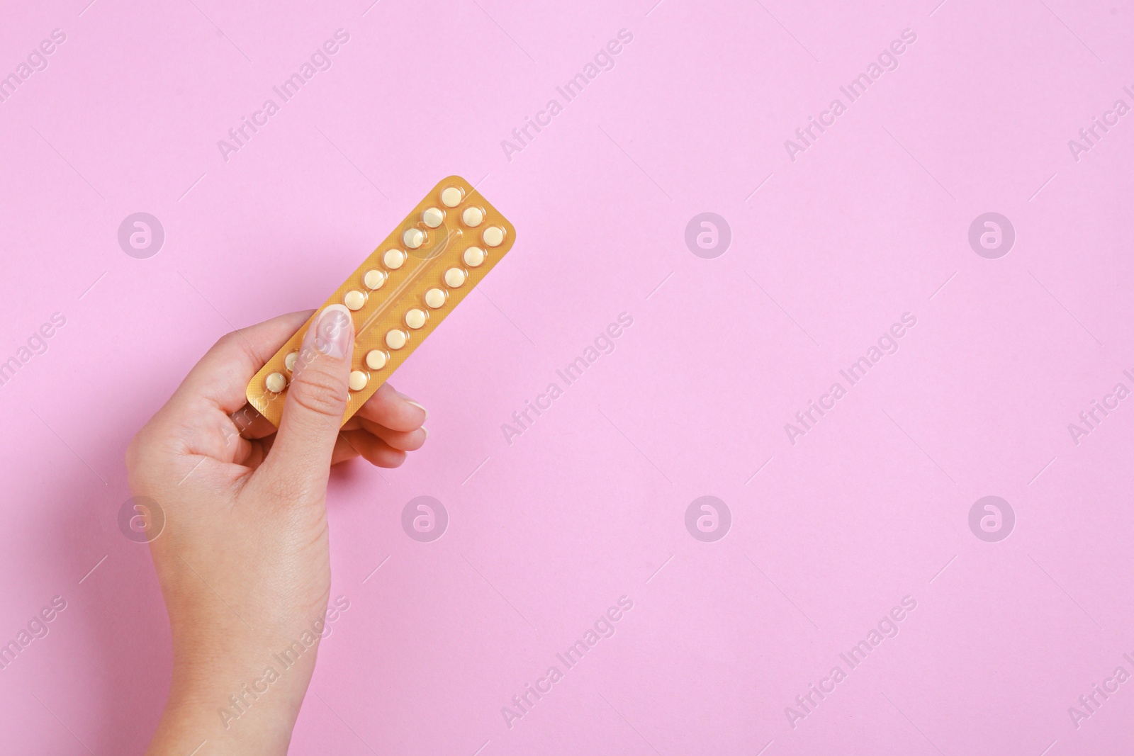 Photo of Woman holding blister with birth control pills on pink background, top view. Space for text
