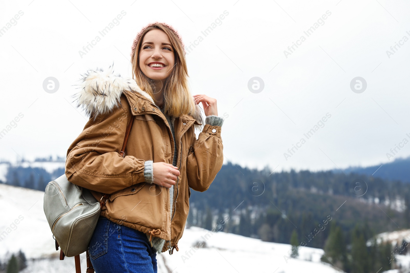 Photo of Young woman in warm clothes near snowy hill, space for text. Winter vacation