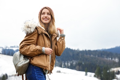 Young woman in warm clothes near snowy hill, space for text. Winter vacation