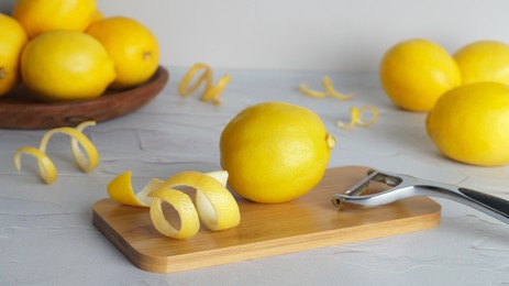 Photo of Wooden board, lemons, peeler and fresh rind on white textured table