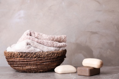 Photo of Different soap bars and basket with towels on table. Space for text