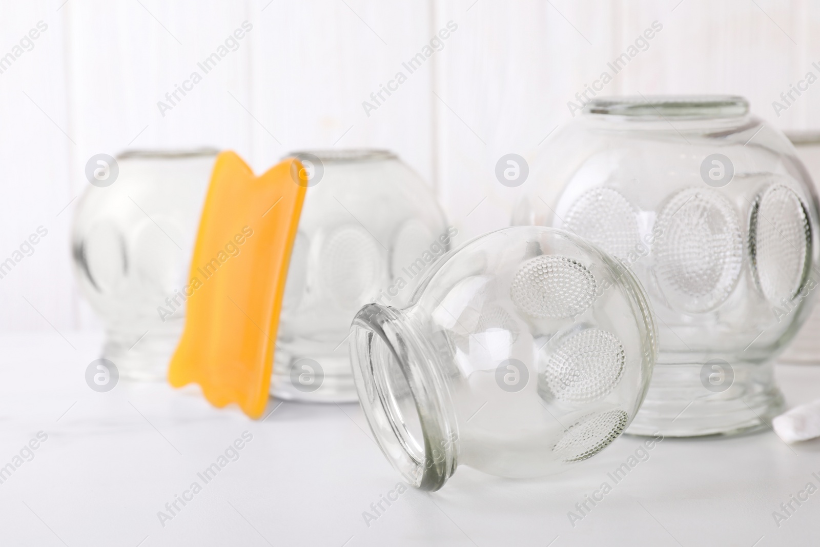 Photo of Glass cups and gua sha on white table, closeup. Cupping therapy