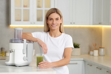 Photo of Happy woman with glass of fresh celery juice at table in kitchen