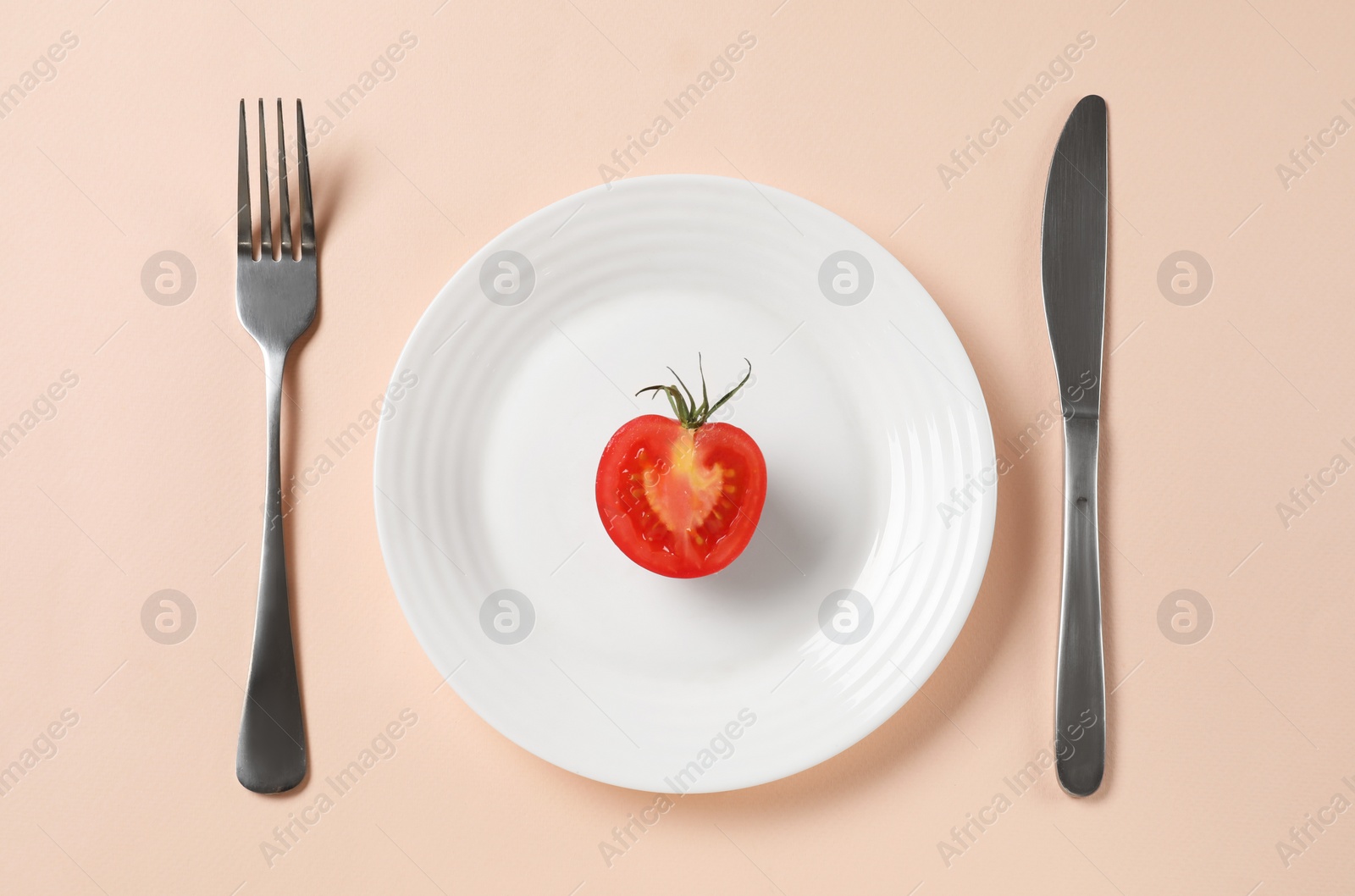 Photo of Plate with half of tomato and cutlery on beige background, flat lay. Diet concept