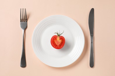 Plate with half of tomato and cutlery on beige background, flat lay. Diet concept