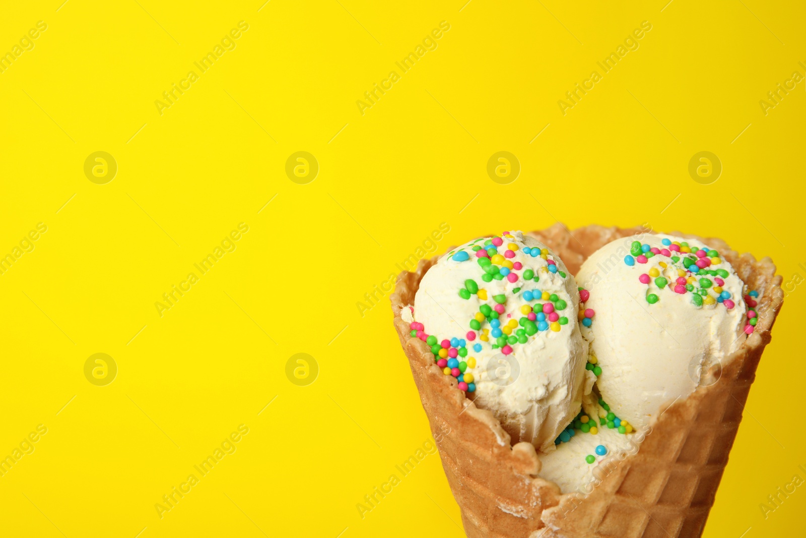 Photo of Delicious ice cream with sprinkles in waffle cone on color background, space for text