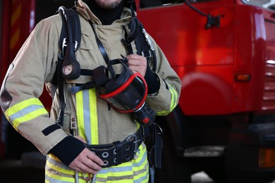 Photo of Firefighter in uniform with mask near red fire truck at station, closeup