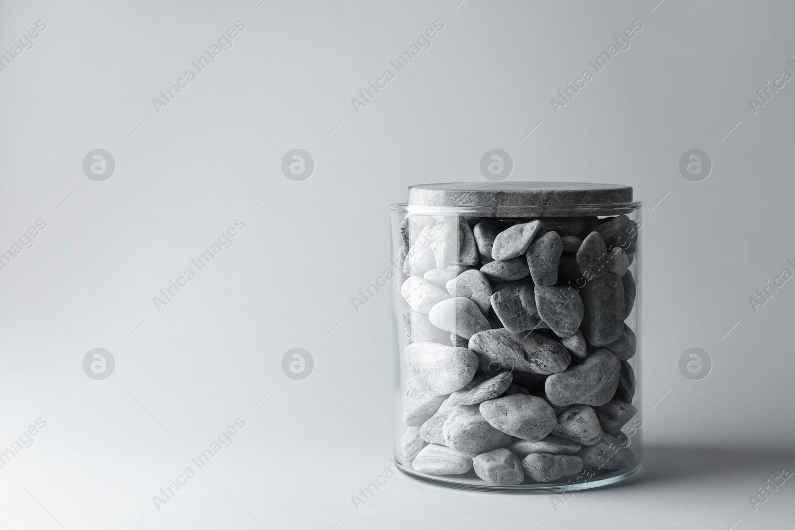 Photo of Presentation for product. Glass container with stones on light grey background. Space for text