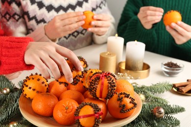 Friends decorating fresh tangerines with cloves at light table, closeup. Making Christmas pomander balls