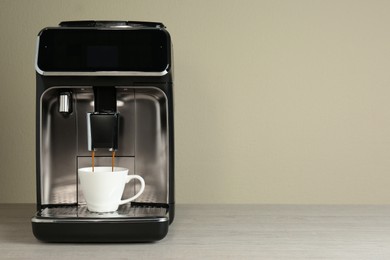 Photo of Modern espresso machine pouring coffee into cup on wooden table near beige wall. Space for text