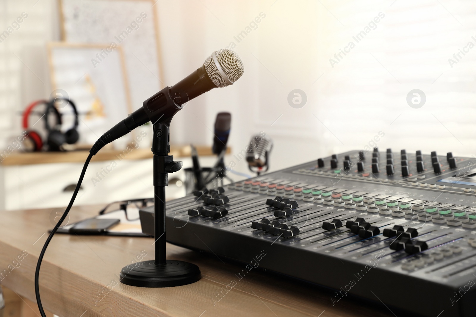 Photo of Microphone and professional mixing console on wooden table in radio studio