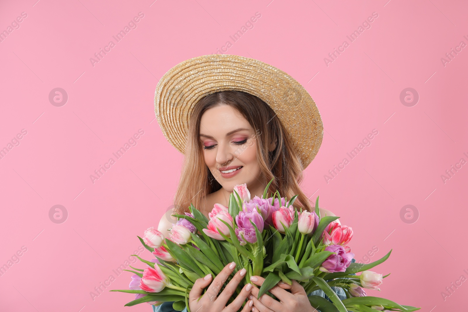 Photo of Happy young woman in straw hat holding bouquet of beautiful tulips on pink background