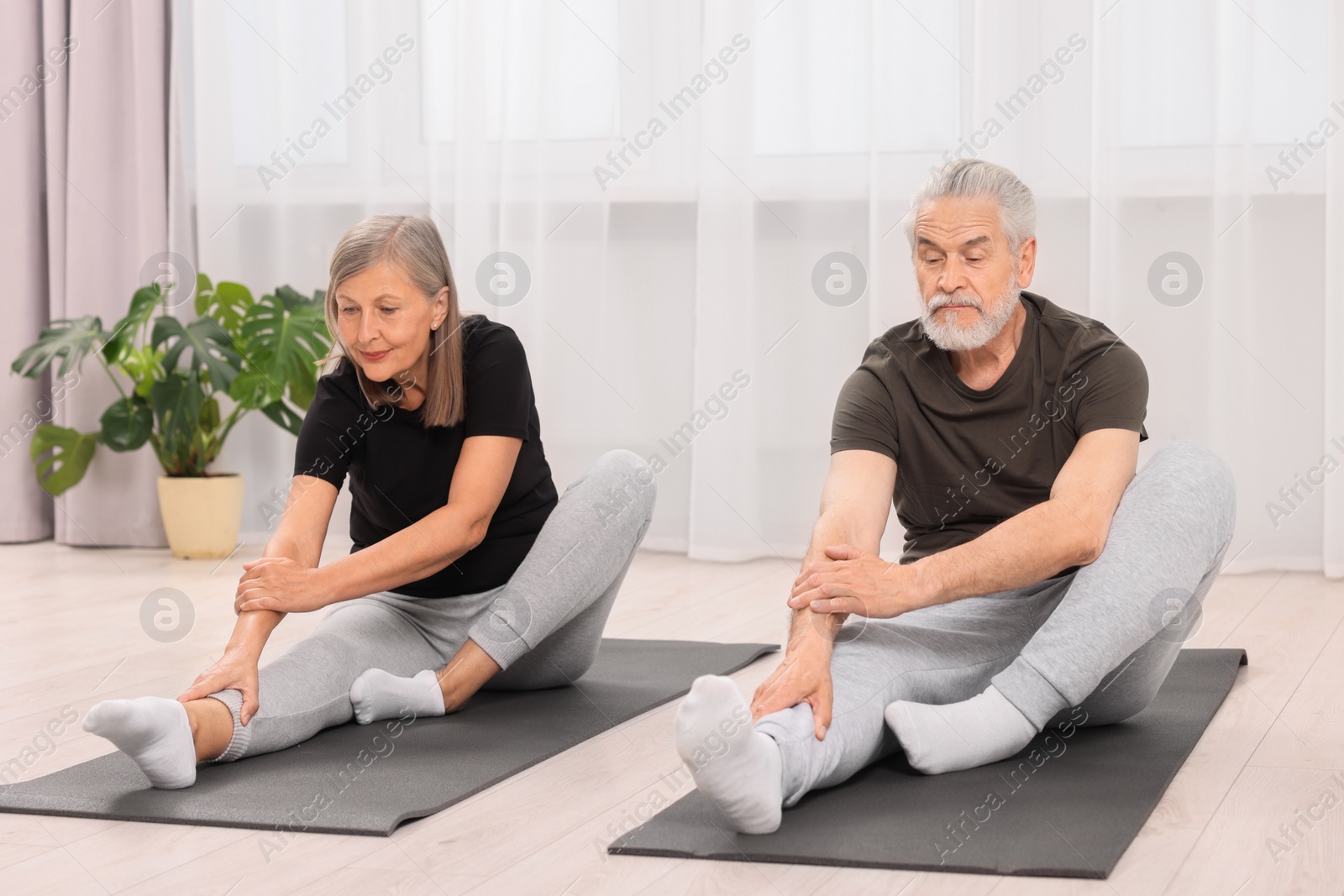 Photo of Senior couple practicing yoga on mats at home
