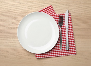 Photo of Stylish ceramic plate, napkin and cutlery on wooden background, flat lay