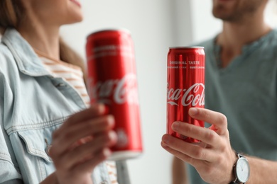 Photo of MYKOLAIV, UKRAINE - NOVEMBER 28, 2018: Young couple with Coca-Cola cans indoors, closeup