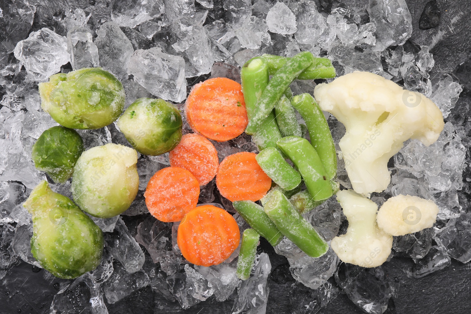 Photo of Different frozen vegetables and ice on black table, flat lay