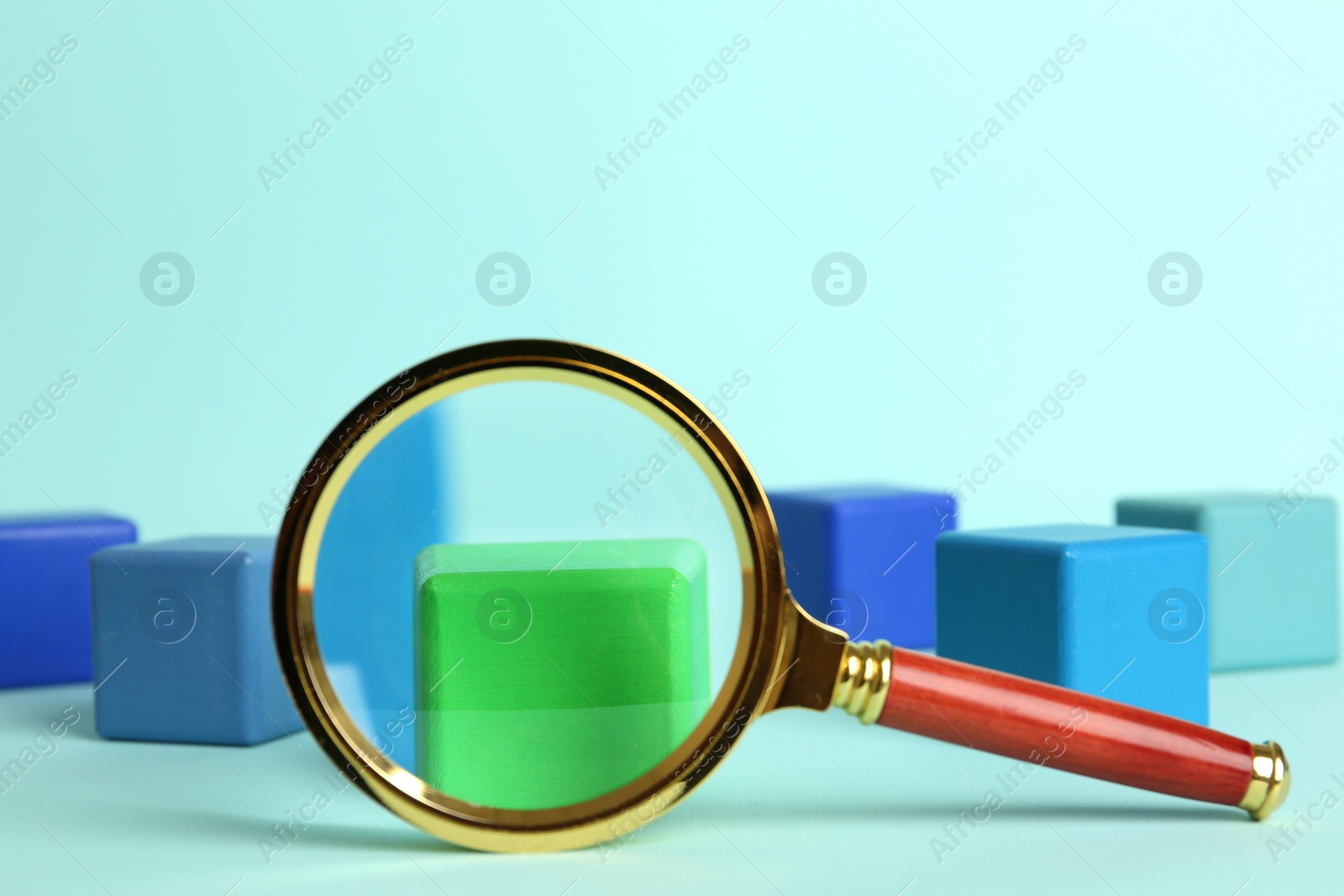 Photo of Magnifying glass and colorful cubes on light blue background. Search concept