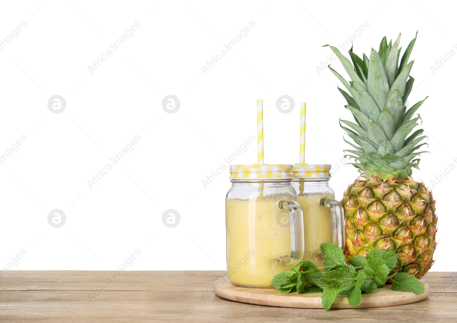 Photo of Tasty pineapple smoothie in mason jars and fruit on wooden table against white background. Space for text