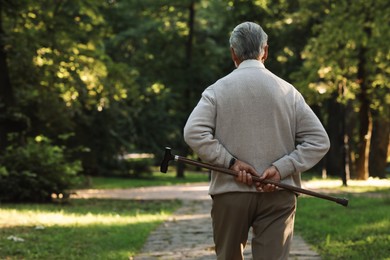 Photo of Senior man with walking cane in park, back view. Space for text