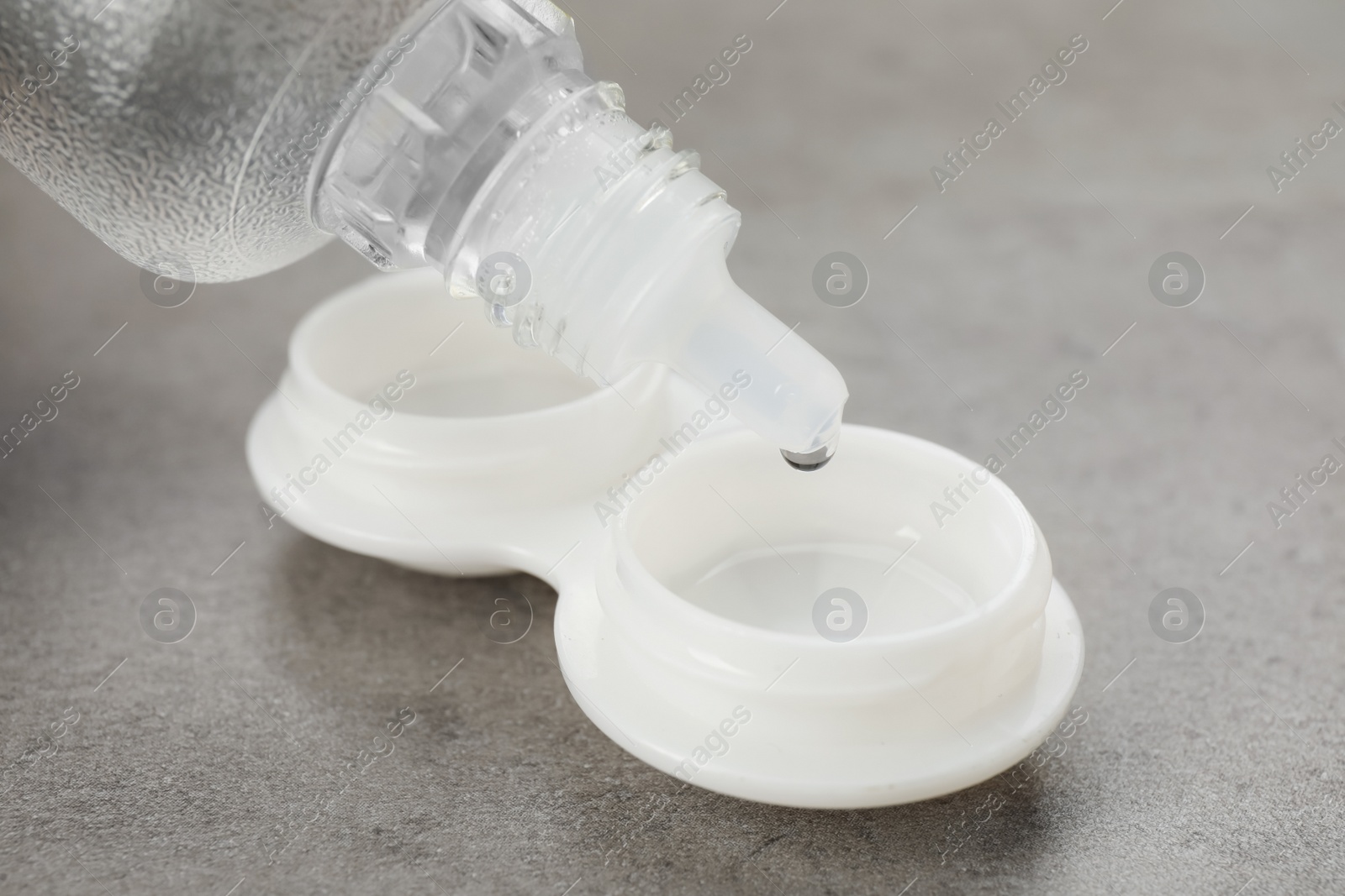 Photo of Dripping solution into case with contact lenses on grey table, closeup