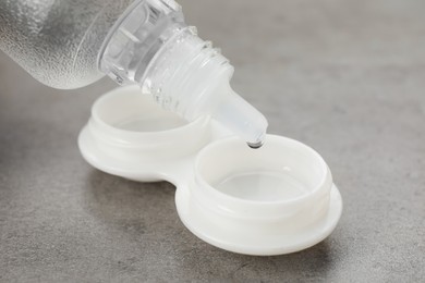 Dripping solution into case with contact lenses on grey table, closeup