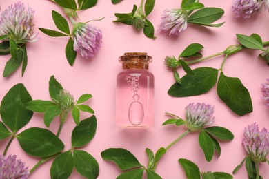 Beautiful clover flowers and bottle of essential oil on pink background, flat lay