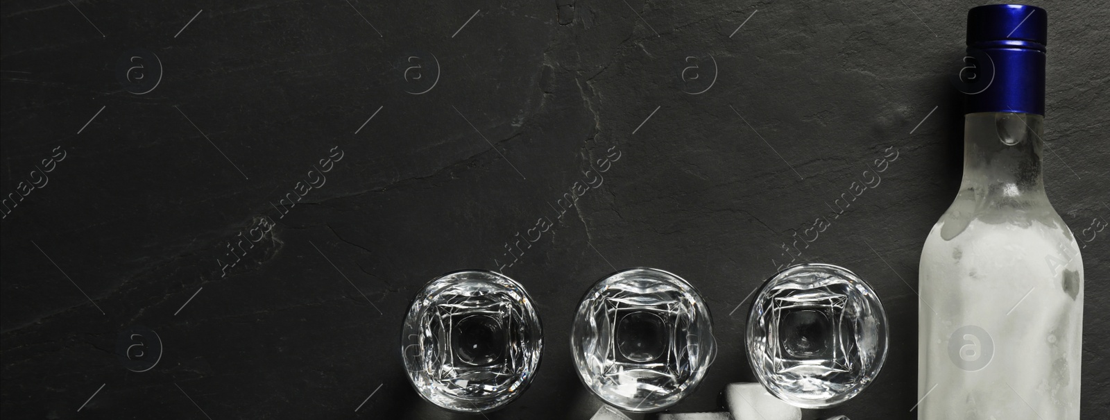 Image of Bottle of vodka, shot glasses and ice cubes on black table, flat lay with space for text. Banner design