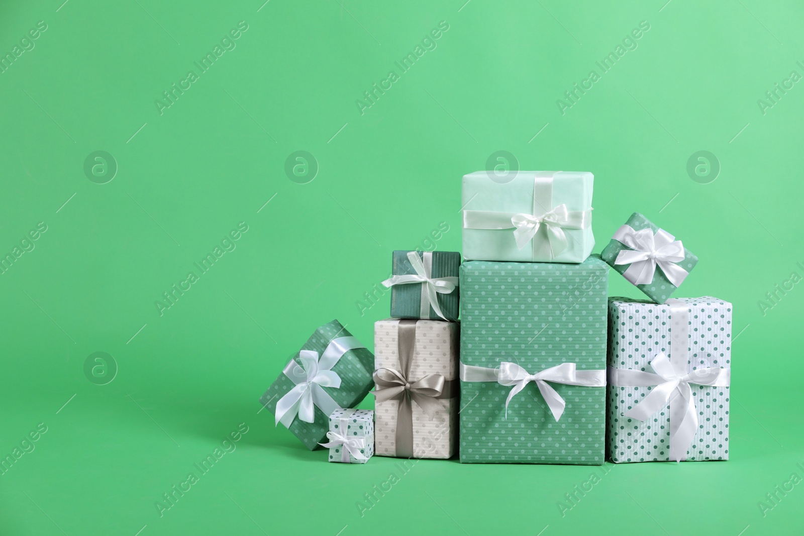 Photo of Many beautifully wrapped gift boxes on green background. Space for text