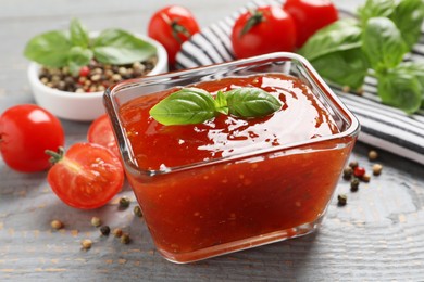 Photo of Spicy chili sauce with basil on grey wooden table, closeup