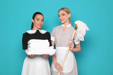 Photo of Young chambermaids with stack of clean towels and mop on color background