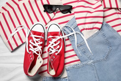 Pair of stylish red shoes, clothes and sunglasses on white fabric, flat lay