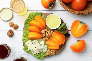 Delicious persimmon, blue cheese, nuts and honey served on white wooden table, flat lay