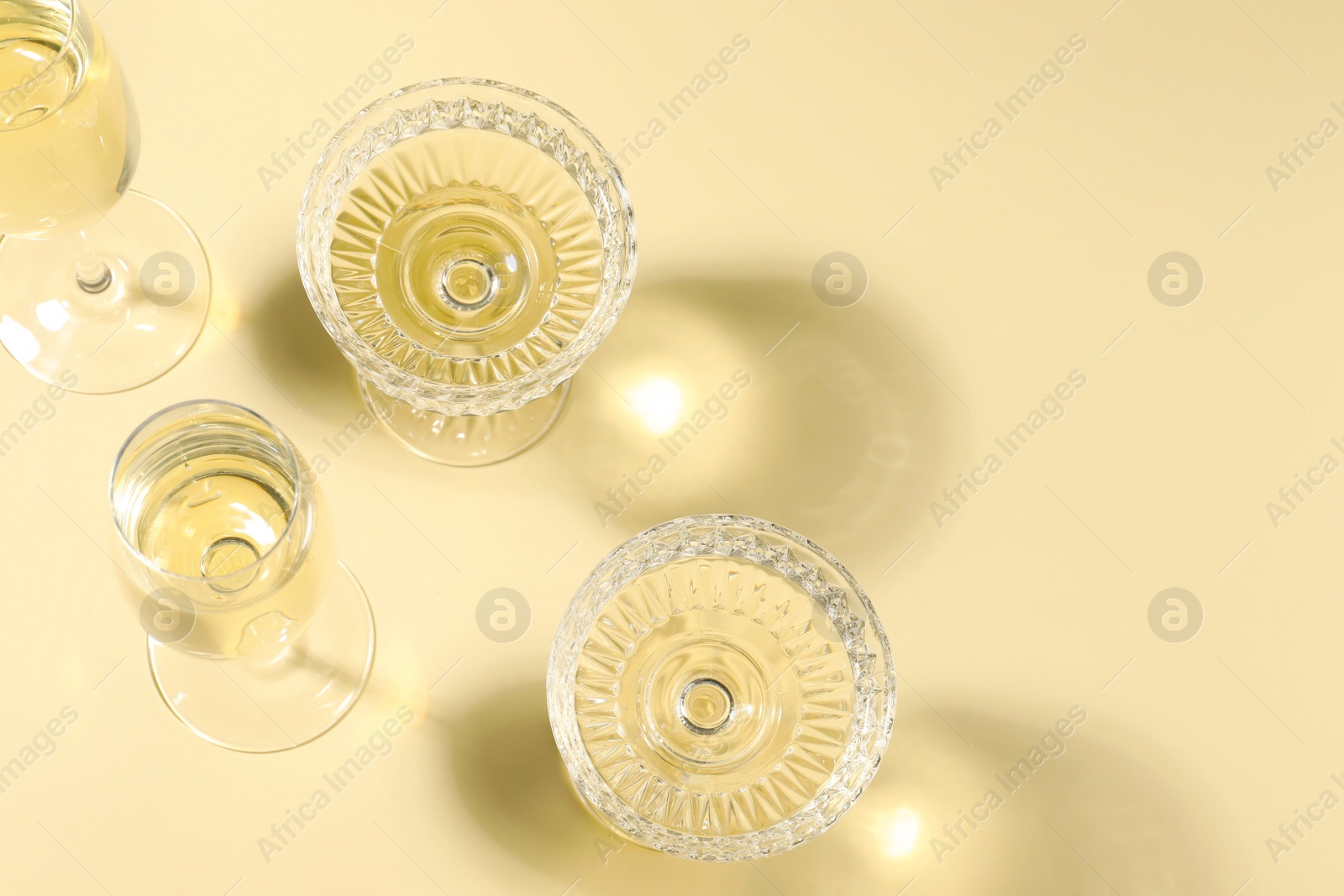 Photo of Glasses of delicious sparkling wine on light yellow background, above view. Space for text