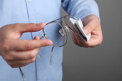 Photo of Woman cleaning glasses with microfiber cloth on light gray background, closeup