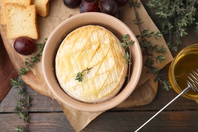 Photo of Tasty baked camembert in bowl, thyme honey, croutons and grapes on wooden table, flat lay