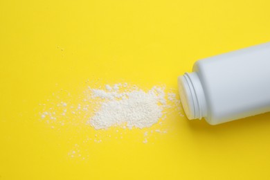 Bottle and scattered dusting powder on yellow background, top view. Baby cosmetic product