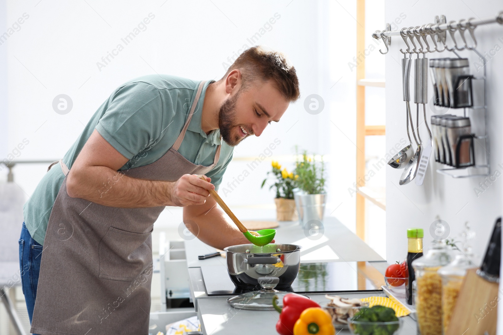 Photo of Young man cooking delicious soup in kitchen