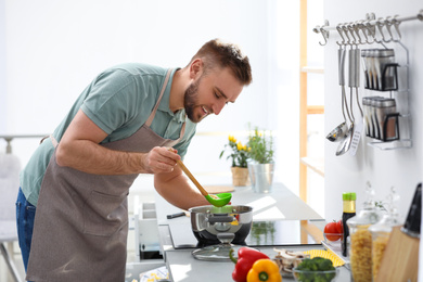 Young man cooking delicious soup in kitchen