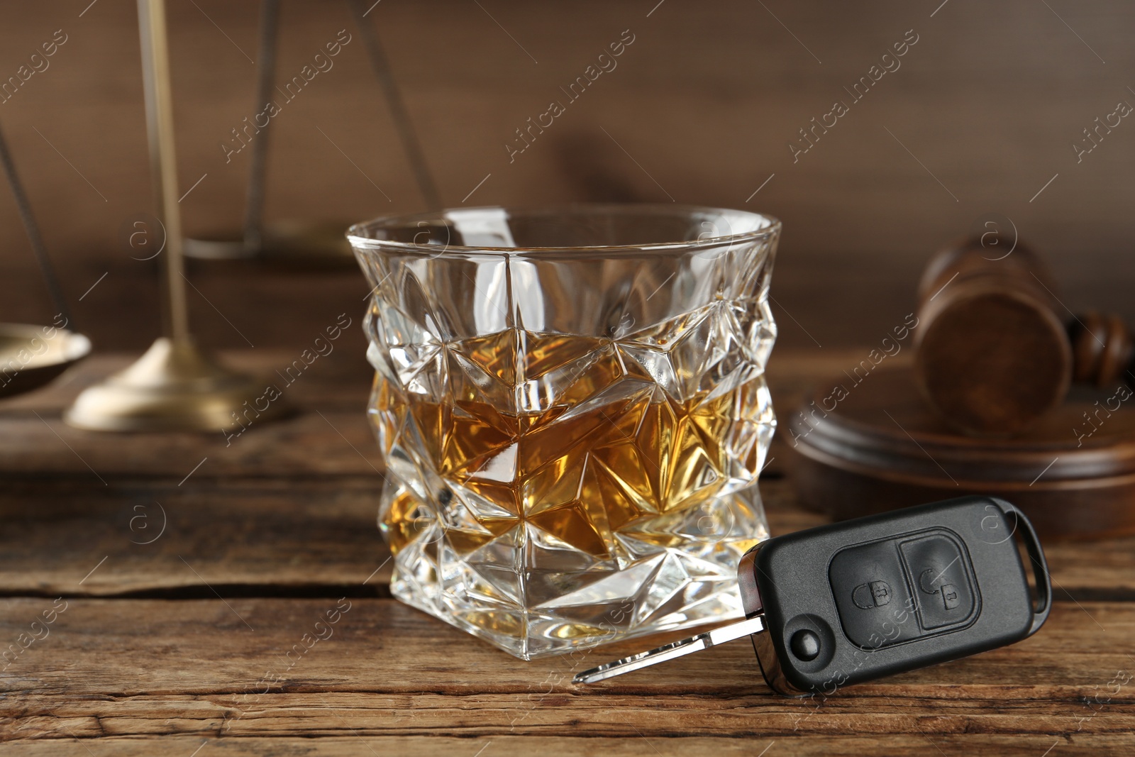 Photo of Car key, glass of alcohol near gavel on wooden table. Dangerous drinking and driving