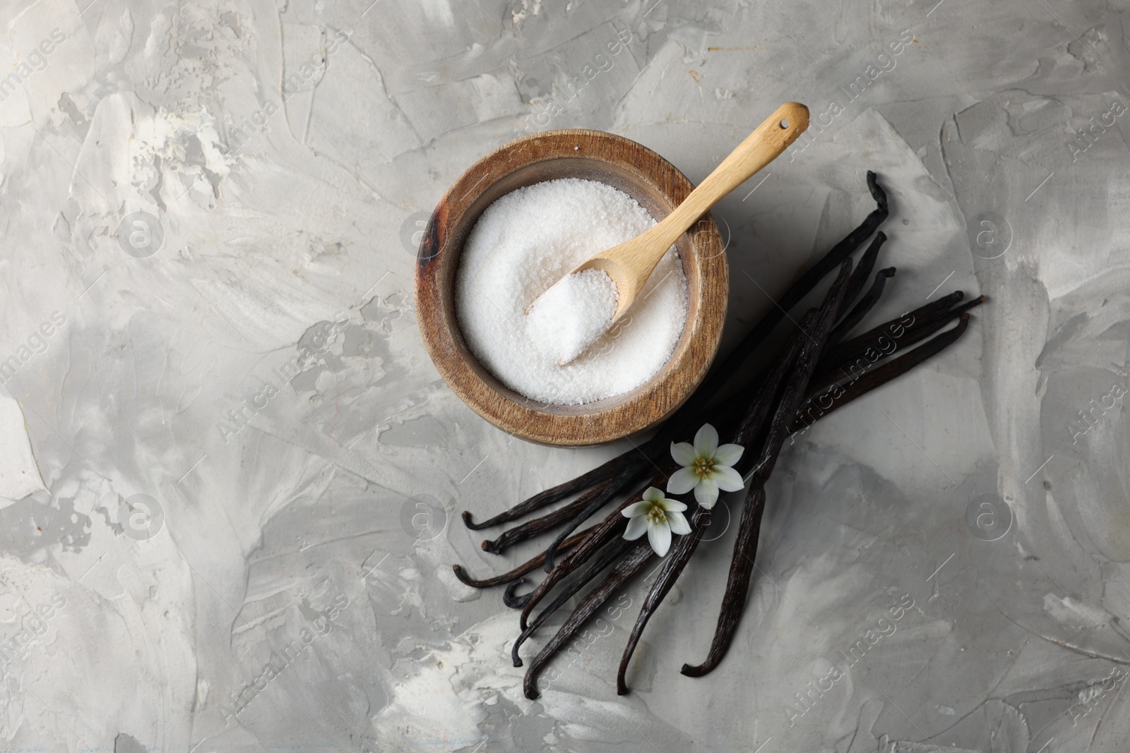 Photo of Sugar in bowl, vanilla pods and flowers on grey textured table, flat lay